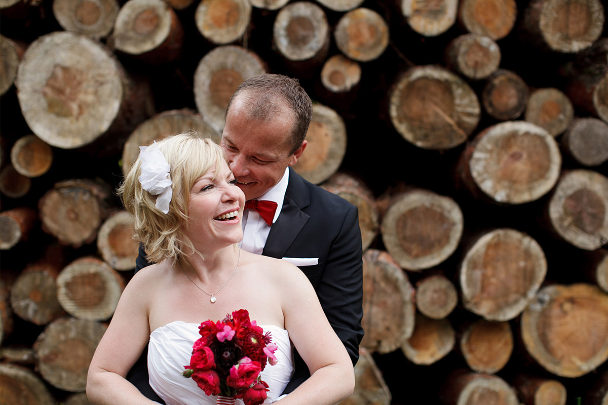 Brautpaarfoto vor gestapelten Baumstämmen bei Schloss und Gut Liebenberg Hochzeit, Brandenburg © Hochzeitsfotograf Berlin hochzeitslicht